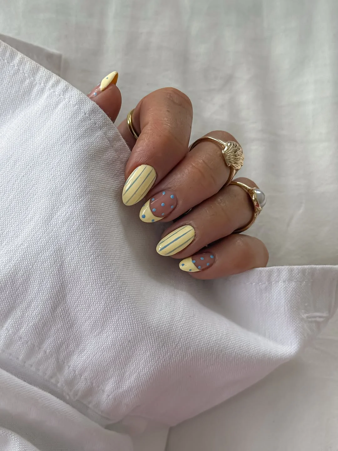 Mix-and-match манікюр у butter yellow з тонкими блакитними смужками на одних нігтях і жовтим французьким краєм з блакитним горошком на нюдовій базі на інших, середня довжина овалу